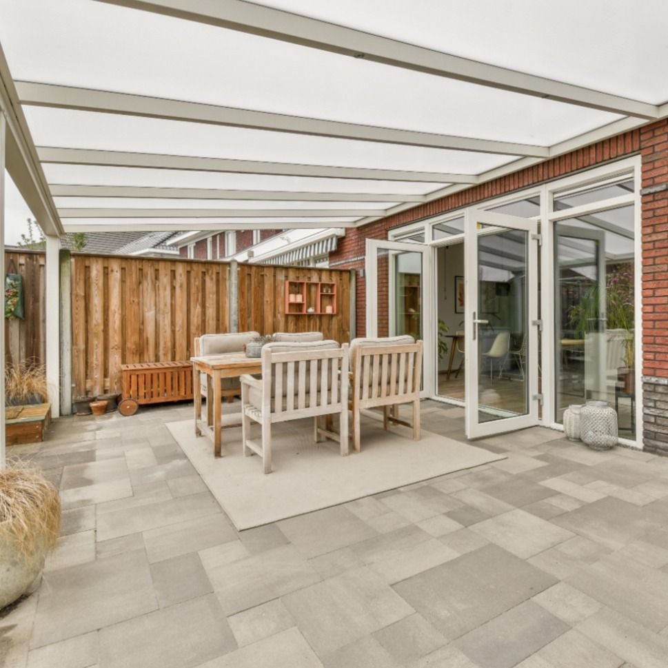 Patio with a gray tiled floor, dining set under a white canopy, and glass doors leading to a brick house.