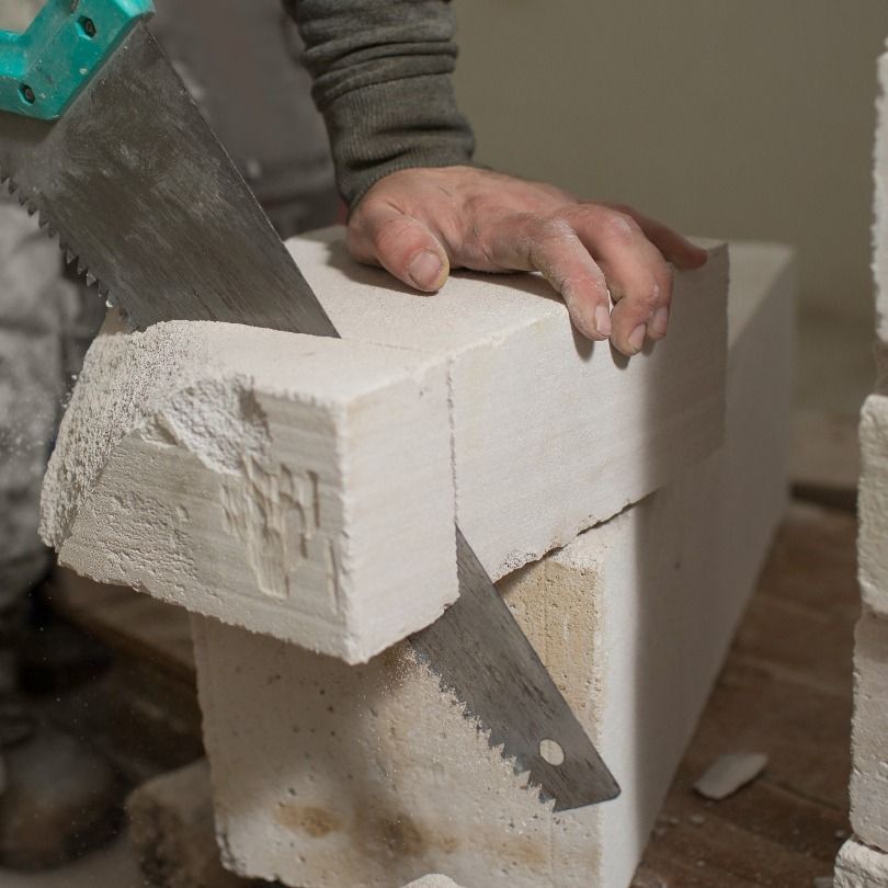A person sawing a white brick with a hand saw. The brick is resting on other bricks.