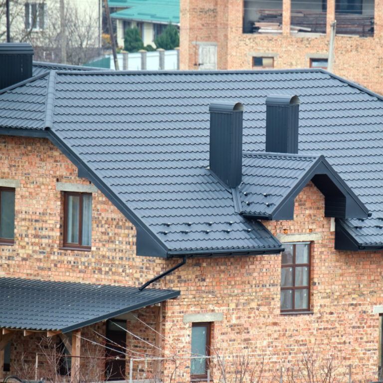 Brick house with a dark gray metal roof. Two black chimneys stand out.