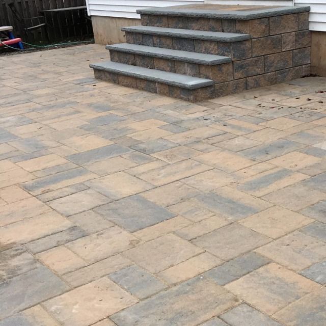 Brick patio with matching steps leading up to a house; beige and gray stone pavers.