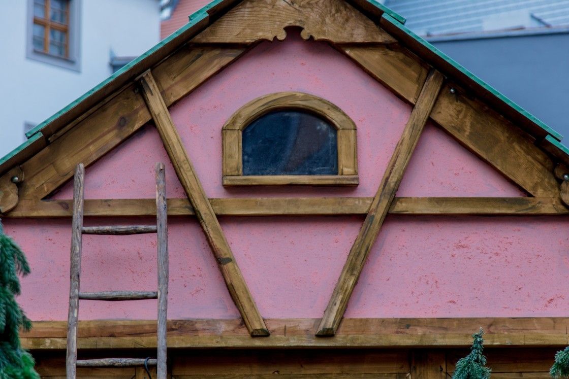 A wooden ladder is hanging from the roof of a pink building.