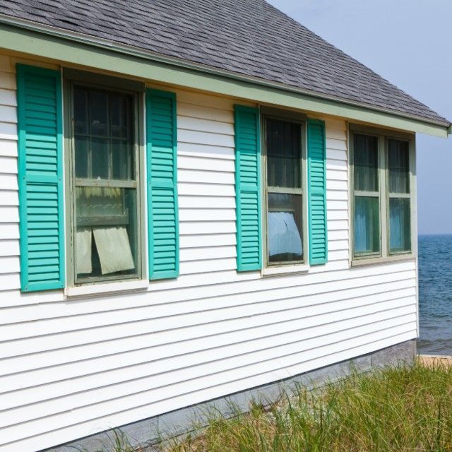 White beach house with teal shutters and windows overlooking the ocean.