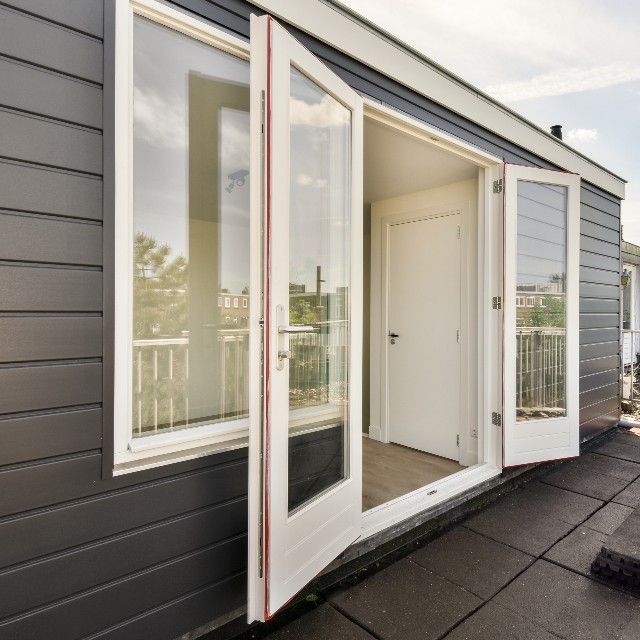 White French doors and a window on a grey-sided building open onto a flat, tiled rooftop.