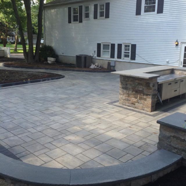A white house with black shutters is behind a brick patio