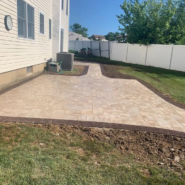 A brick patio is being built in the backyard of a house.