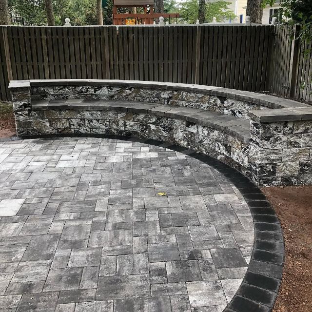 A brick patio with a stone wall and a bench