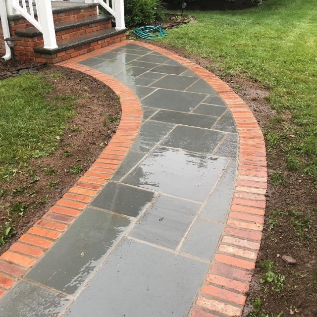 A brick walkway with a hose on the side of it leading to a porch.