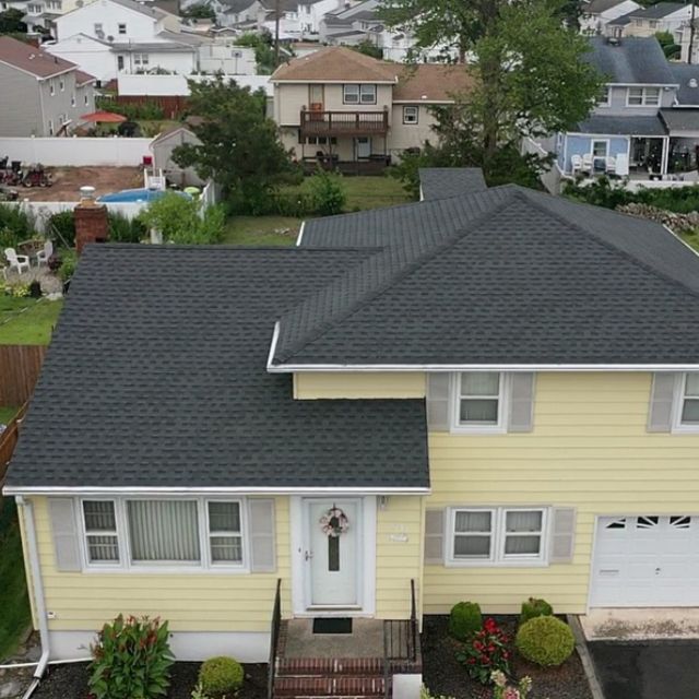 An aerial view of a yellow house with a black roof