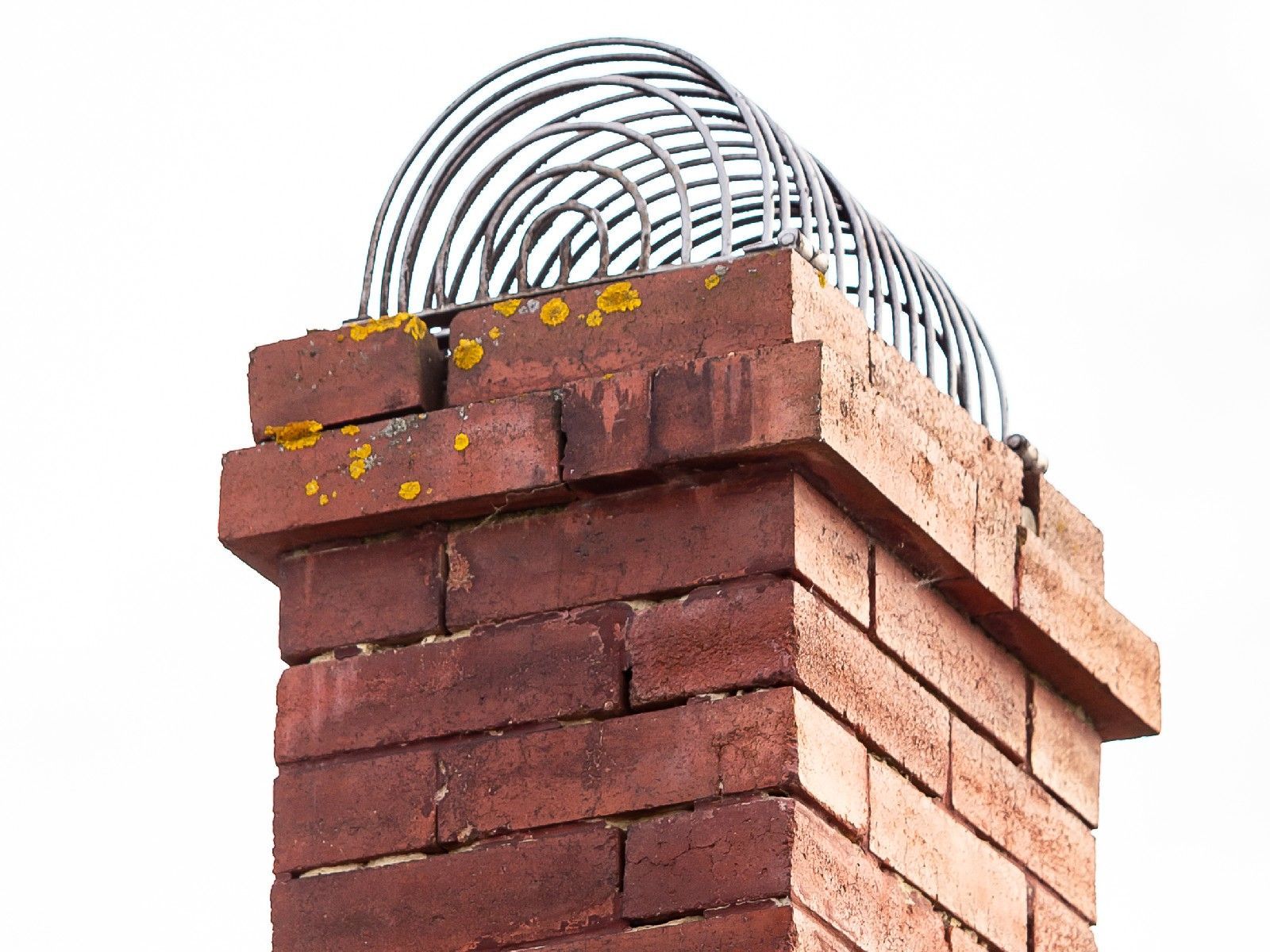 A brick chimney with a barbed wire fence on top of it