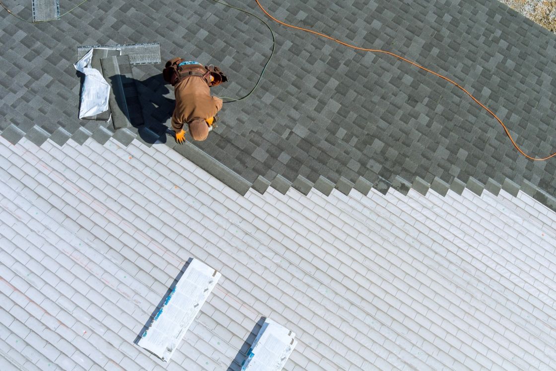 An aerial view of a man installing shingles on a roof.