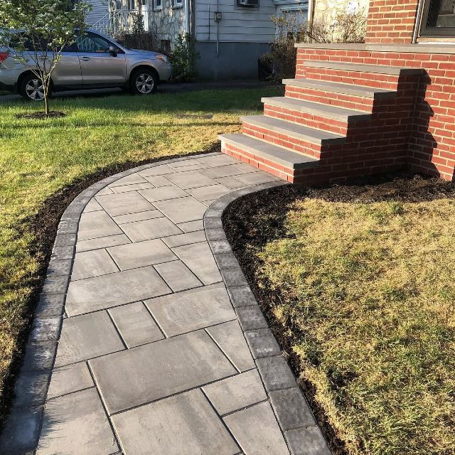 A walkway leading to a brick house with stairs and a car parked in the background.