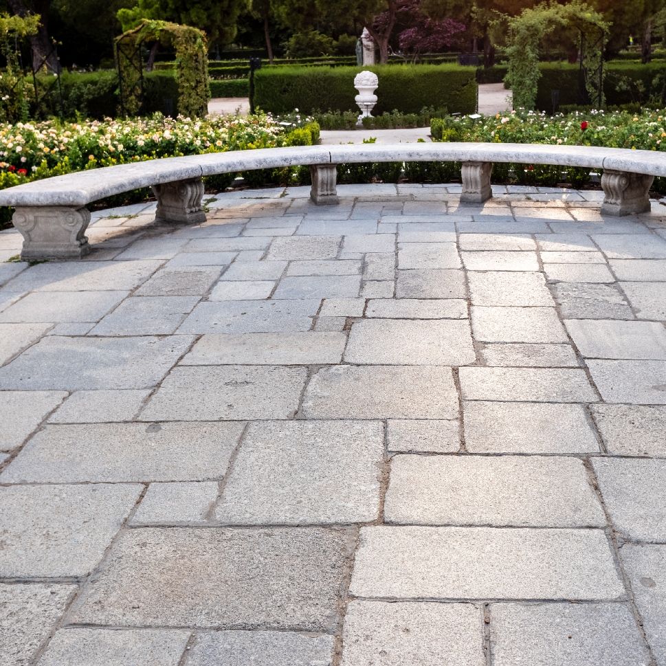 A circular stone bench in a park with a statue in the background