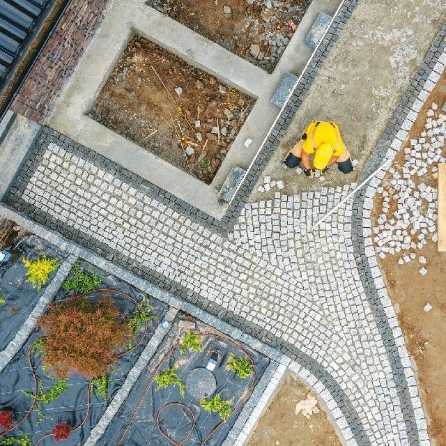 An aerial view of a man in a yellow jacket working on a cobblestone walkway.