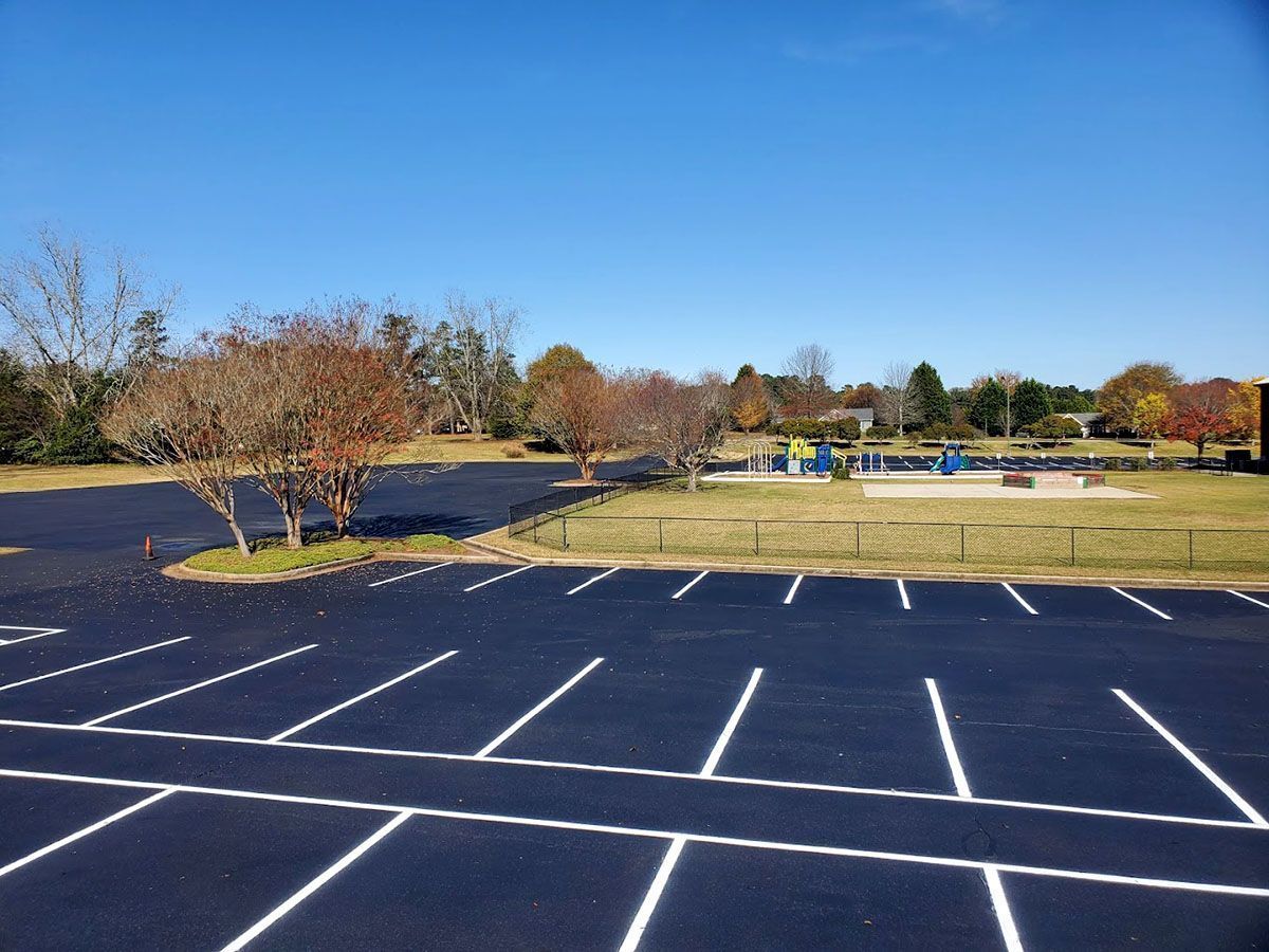 A parking lot with a playground in the background on a sunny day.