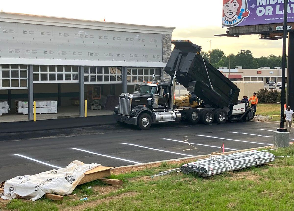 A dump truck unloading asphalt in front of an under-construction building