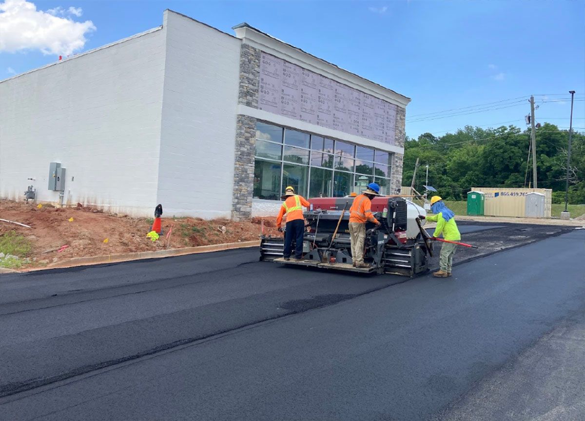 A group of workers paving a road in front of a building