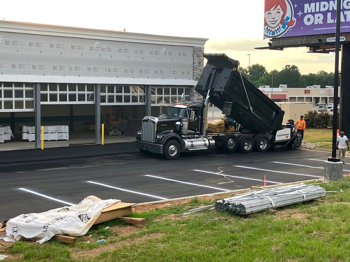 A dump truck is unloading asphalt in a parking lot in front of an under-construction building