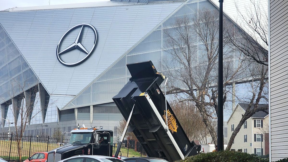 A dump truck is parked unloading asphalt in front of a commercial building