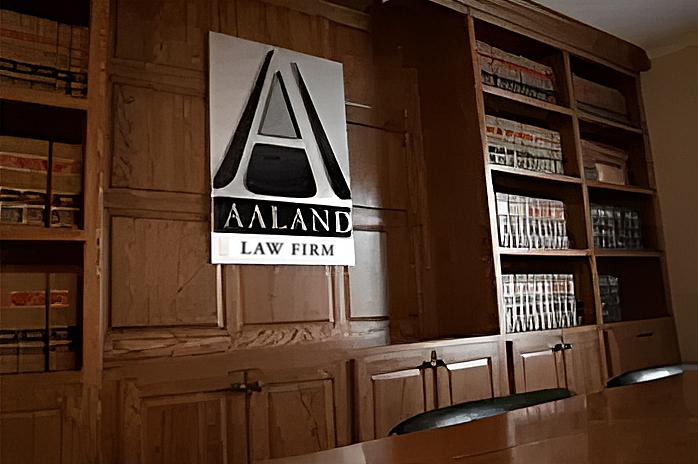 Aaland Law Firm sign on wood-paneled office wall beside bookshelves and conference table.