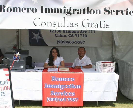 Two people sitting at a table with a sign that says Romero Immigration services