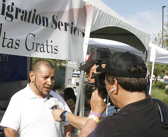 A man is being interviewed in front of a sign that says migration services