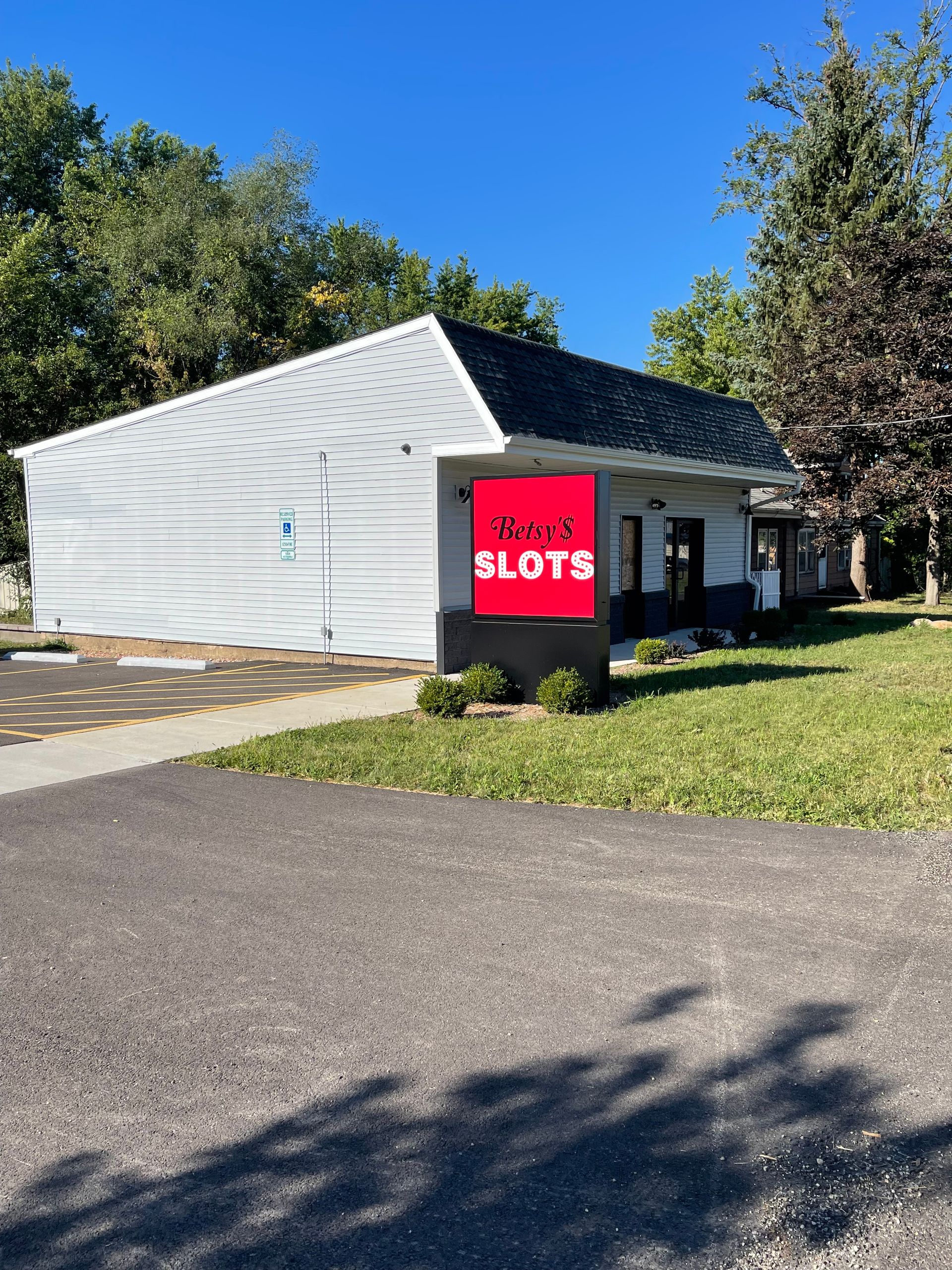 A gaming parlor building with a red Slots sign. Exterior shot with asphalt and green grass.