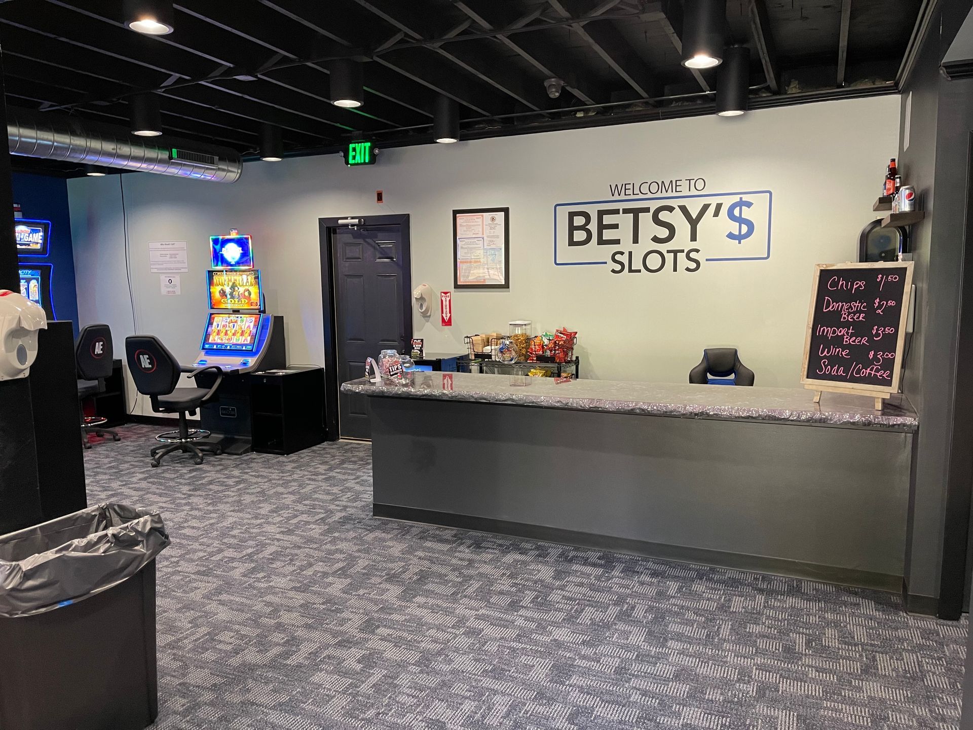 Interior view of Betsy's Slots, a gaming area with slot machines, a counter, and a trash can.