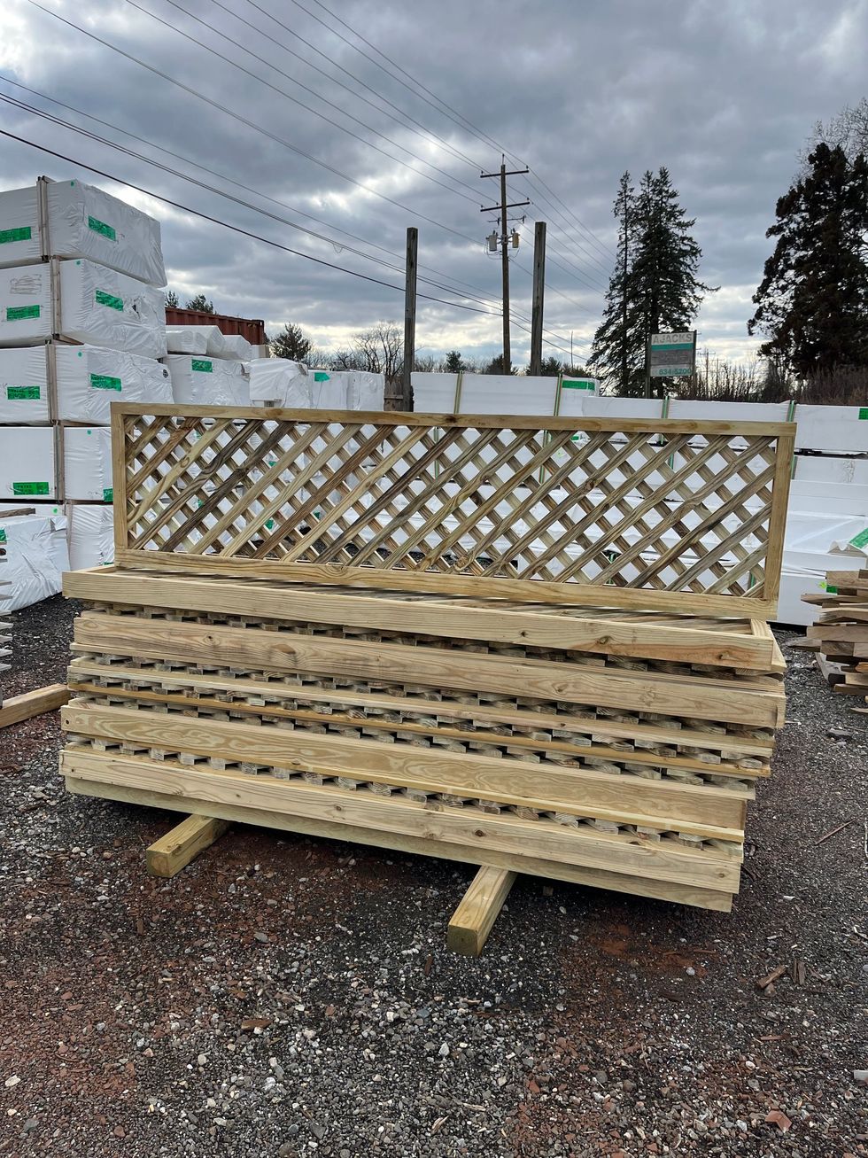 A stack of light-colored wooden lattice panels sitting on wooden supports in an outdoor lumber yard.