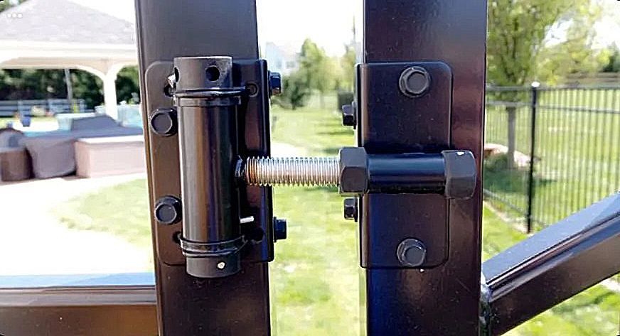 Black adjustable gate hinge mounted on horizontal metal rails, featuring a central tension bolt and mounting plates.