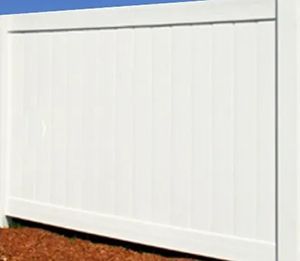 A section of a white vinyl privacy fence with vertical panels, standing against a blue sky over brown mulch.