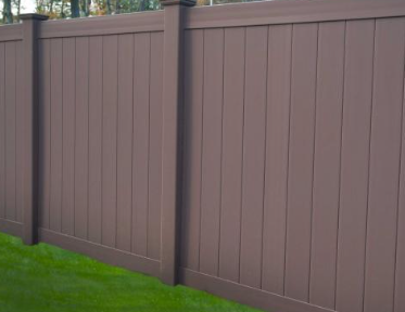 A brown, vertical-slat privacy fence made of composite material, set against a green lawn.