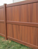 A close-up of a brown, wood-grain patterned privacy fence with vertical panels and horizontal support rails.