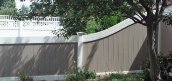 A beige vinyl privacy fence features a white curved top rail section next to a white lattice-topped panel in a yard.
