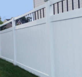 A tall white vinyl privacy fence with black vertical spindle accents at the top, standing on a green grass lawn.