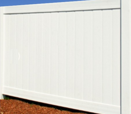 A section of a white vinyl privacy fence with vertical panels, standing against a blue sky over brown mulch.