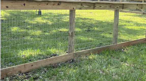 A wooden fence with wire mesh panels installed against a grassy lawn.
