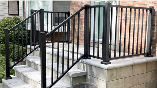 Black metal railing installed on concrete steps leading to a brick house.