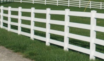 A white, four-rail ranch-style fence borders a green grassy field under a bright sky.