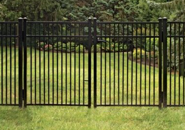 A black metal picket fence with a double gate set in a grassy yard backed by trees and shrubs.