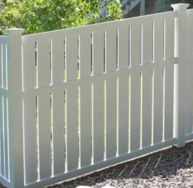 A white vinyl privacy fence with vertical slats and a stepped top design, installed over a bed of gravel.