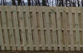 A side-by-side view of a new wooden fence with vertical pickets showing light wood tones against a backdrop of bare trees.