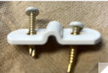 A white, U-shaped cable clamp with two gold screws pre-inserted through the mounting holes, set against a brown background.