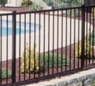 A black metal swimming pool fence installed atop a stone retaining wall in a backyard.