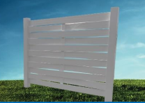 A white horizontal slat privacy fence section stands in a grassy field against a blue sky.