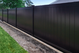 A tall, solid black privacy fence runs along a concrete base beside a patch of green grass.