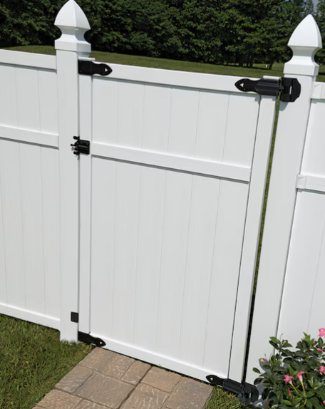 A white vinyl privacy fence with a matching gate featuring black metal hinges and a latch, set on a stone walkway.