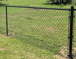 A black chain-link fence stands on a grassy lawn with a black metal post in the foreground.