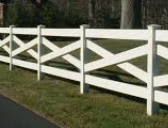A white, four-rail ranch-style fence with X-shaped cross-bracing, positioned along a grassy lawn next to a paved path.