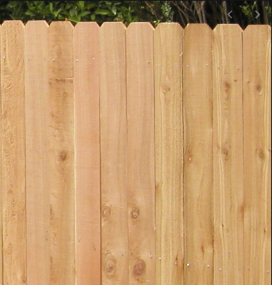 A vertical wooden fence with light-brown planks featuring uniform dog-eared tops.
