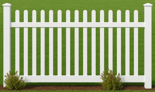 A white vinyl picket fence section with rounded tops, set against a green grass background with small shrubs at the base.